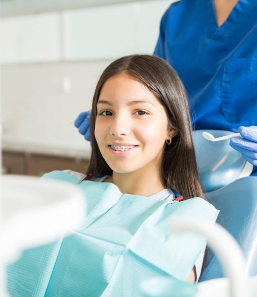 Portrait of smiling teenage girl with braces sitting on chair while dentist standing in clinic